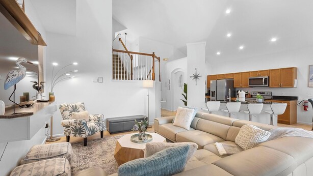 A spacious living room with a large beige sofa, a coffee table, and a staircase leading to an upper floor. - Wish Upon A Palm | Private Pool & Resort Amenities (Kissimmee)