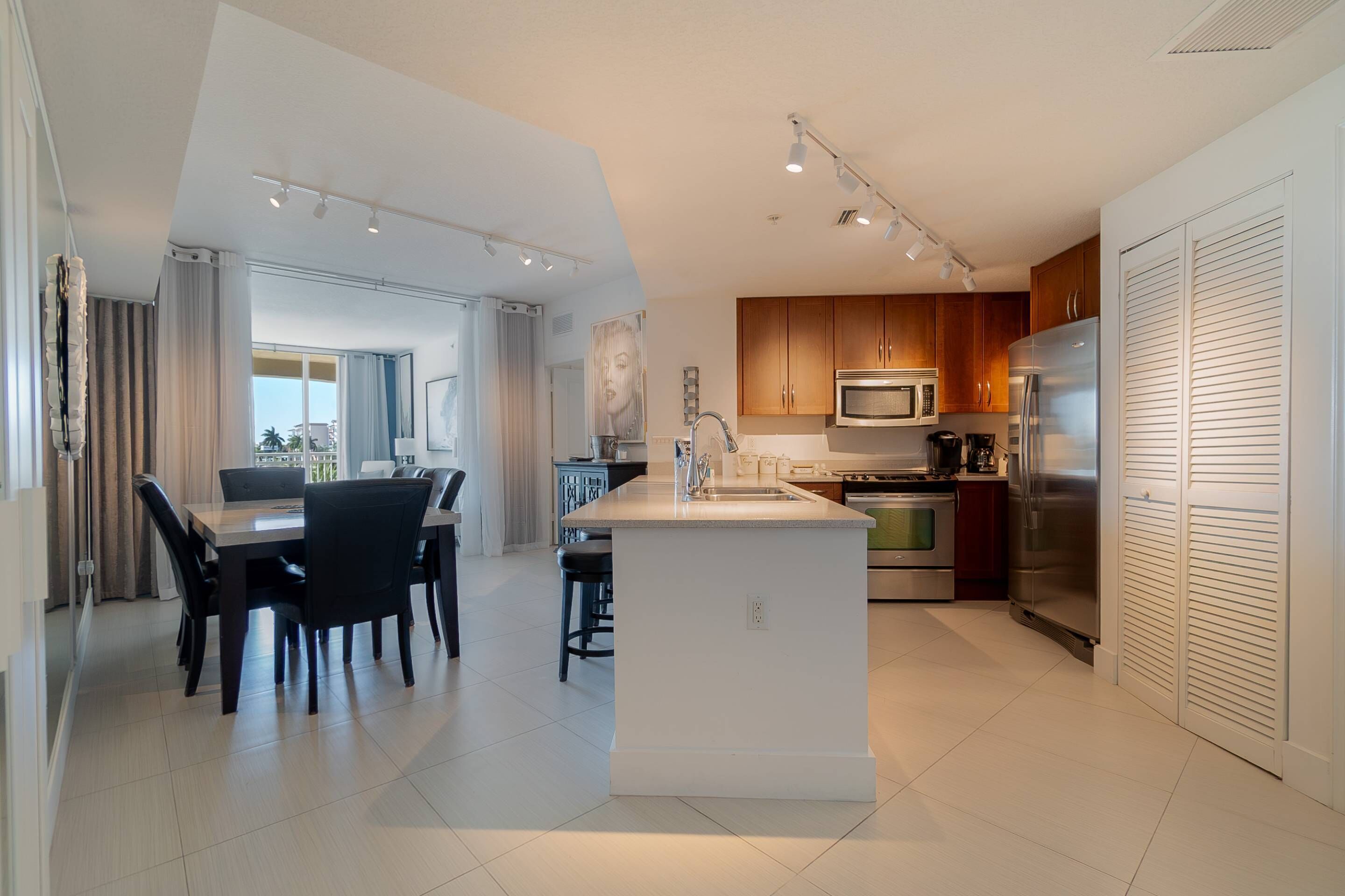 Een moderne keuken met een centraal eiland, roestvrijstalen apparatuur en een eethoek met tafel en stoelen.