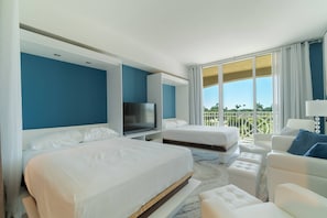 Quarto de hotel com duas camas, televisão, varanda com vista e decoração em tons de branco.