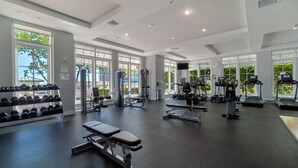 A spacious gym with various exercise equipment, large windows, and a bench.