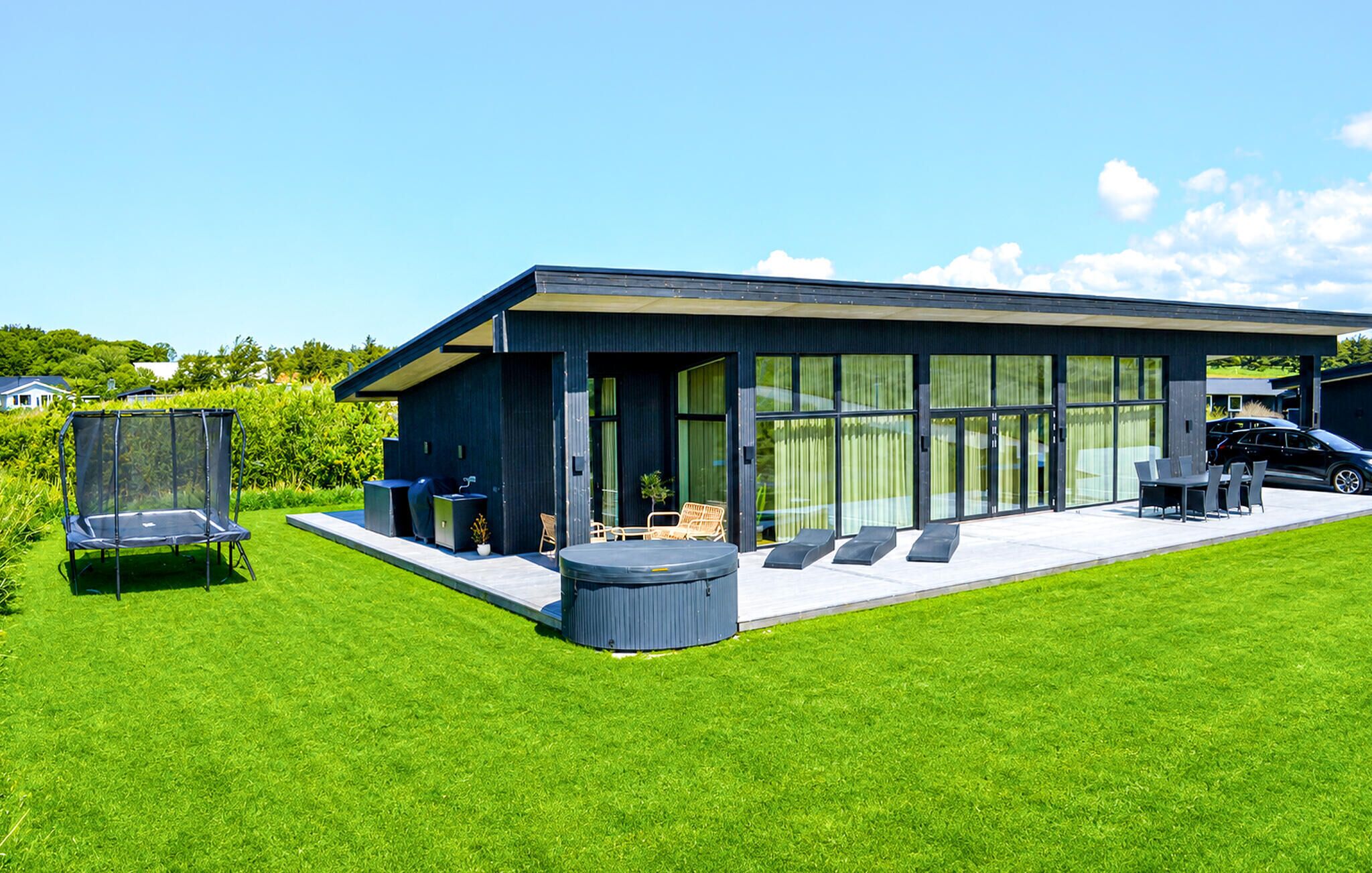 A modern house with a large glass door, outdoor seating, and a trampoline.