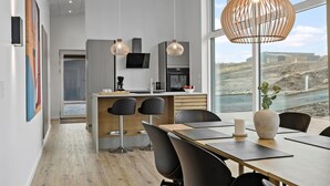 A modern kitchen with a central island, a dining area with a large table and chairs, and a view of the beach through large windows.