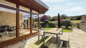 A patio with a table and chairs, a stone floor, and a view of a garden and trees.