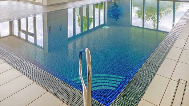 A large indoor swimming pool with clear glass walls, a tiled floor, and a potted plant near the windows.