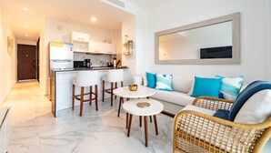 A modern living room with a sofa, two round tables, and a kitchen area with a refrigerator and coffee machine. - Airbn Be Luxe Best Golf  view Cana Rock Star E 304 (Bavaro)