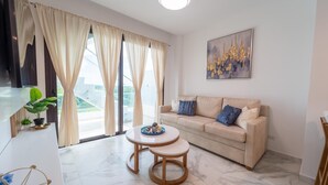 Un salon moderne avec un canapé beige, une table basse ronde et une grande fenêtre avec des rideaux.