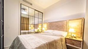 Une chambre d’hôtel avec un grand lit, deux tables de chevet avec des lampes, un miroir et un luminaire au plafond.