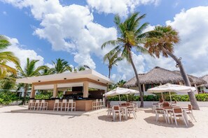 Un área de bar en la playa con asientos al aire libre y construcciones de techo de paja.