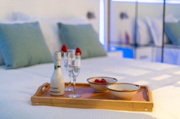 A wooden tray with a bottle of Chenet wine, two glasses, and bowls of strawberries on a bed.