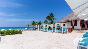 Un resort frente a la playa con cabañas de techo de paja, sillas de descanso y vista despejada del océano.