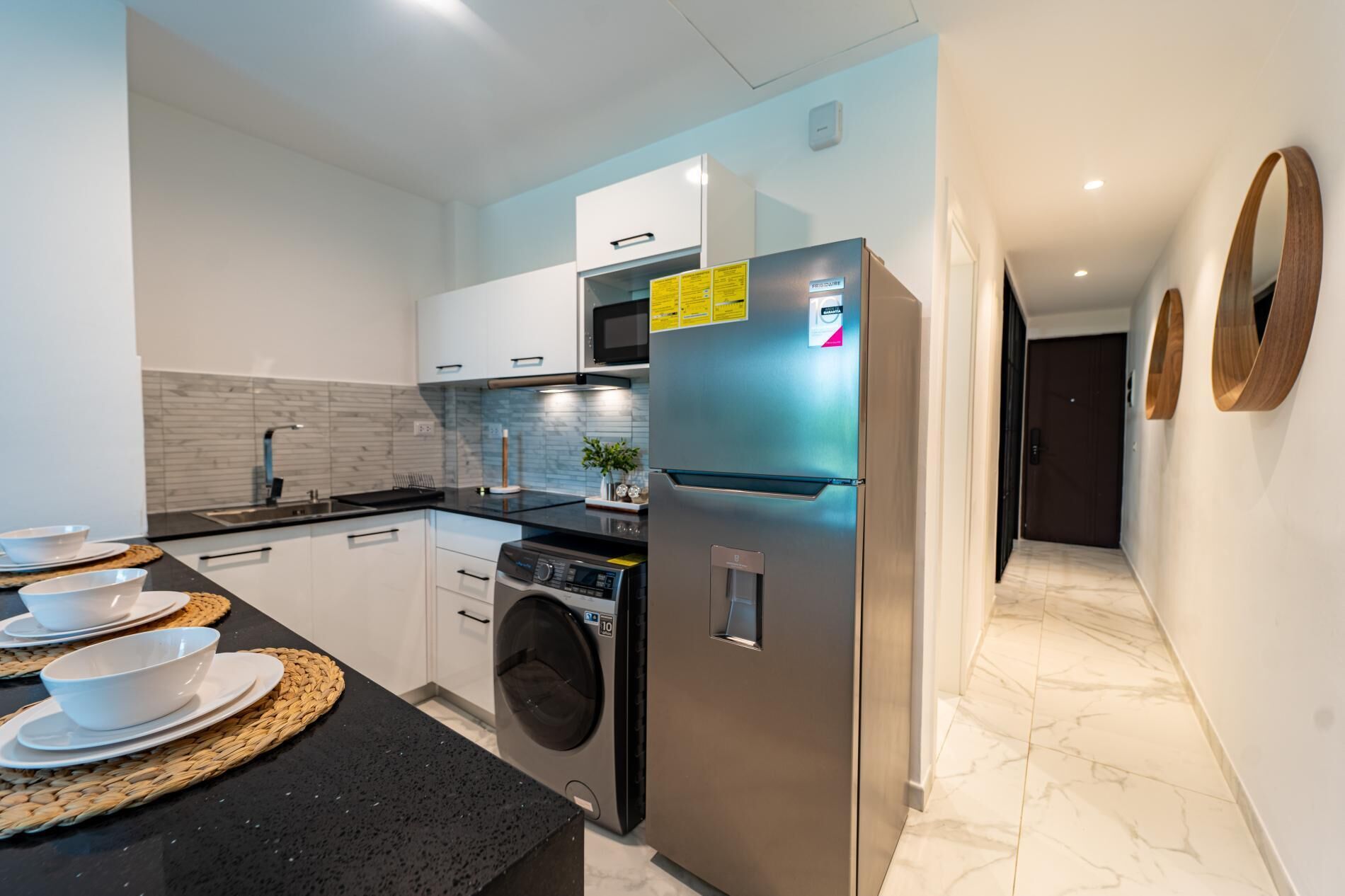 A modern kitchen with a stainless steel refrigerator, a built-in washing machine, and a black countertop.
