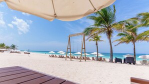 Une plage avec des balançoires, des palmiers et des chaises de plage sous des parasols.