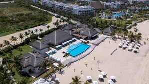 An aerial view of a resort with a large swimming pool, multiple beachside cabanas, and a variety of accommodations including villas and standard rooms.