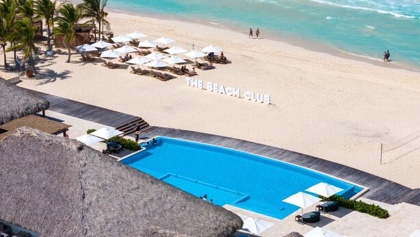 A beach with a pool, umbrellas, and lounge chairs.