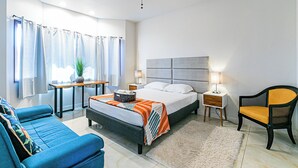 A bedroom with a bed, a blue sofa, a chair, a nightstand, a lamp, and a ceiling fan. - Hilo Manu Iki Guest house (Hilo)
