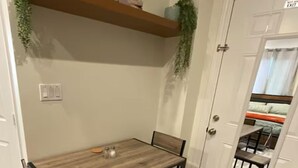 A dining area with a wooden table and chairs, a bench, a shelf with plants, and a door with a view of a bedroom. - Cozy, private full Guesthouse in Bakersfield, CA (Bakersfield)