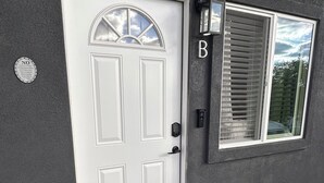 A white door with a window above it, a black doormat, and a small sign on the wall. - Cozy, private full Guesthouse in Bakersfield, CA (Bakersfield)