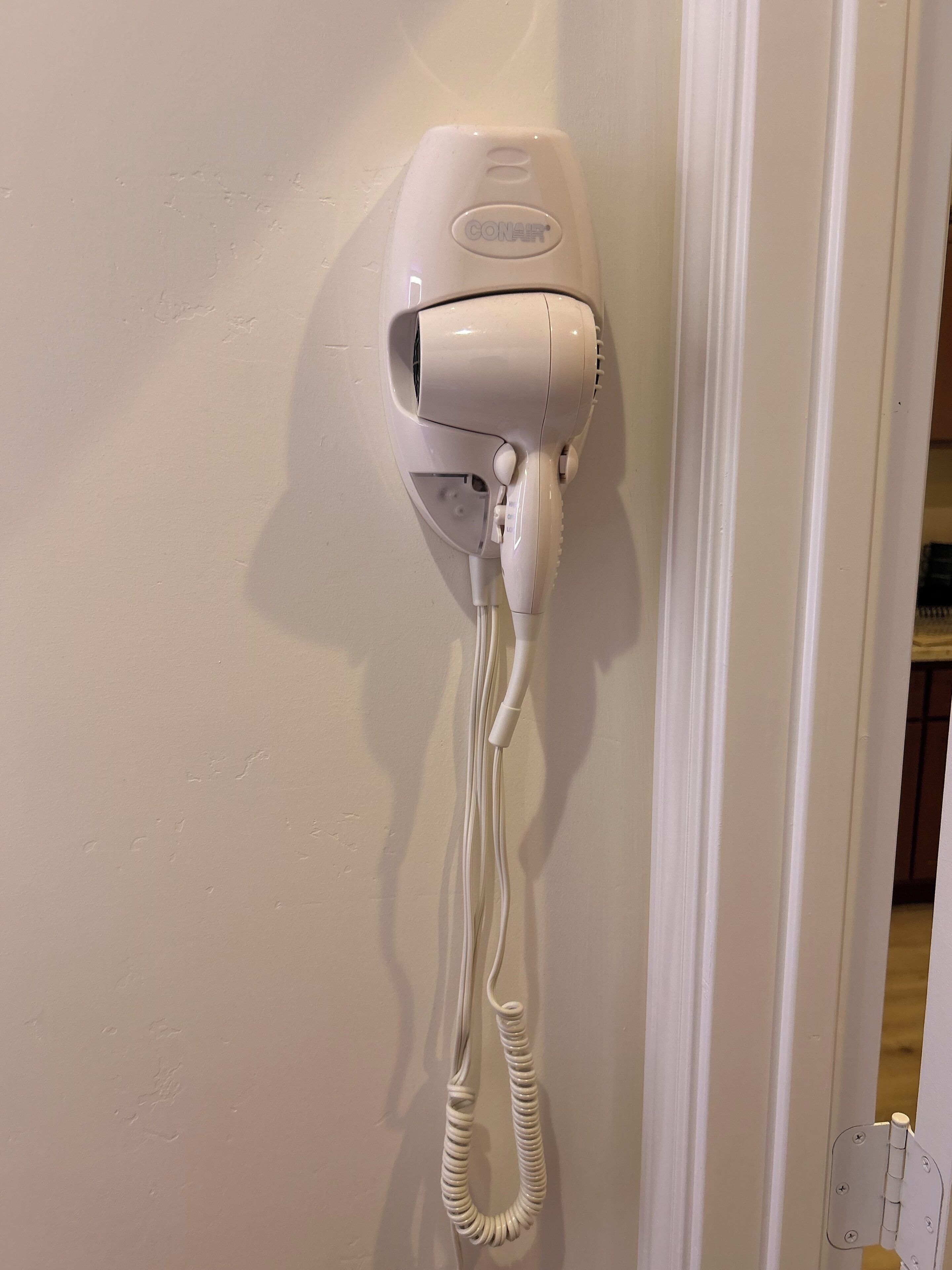 A white hair dryer mounted on a wall with a coiled cord.