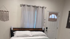 A bedroom with a bed, a window with curtains, a door, and a wall-mounted macrame piece. - Cozy, private full Guesthouse in Bakersfield, CA (Bakersfield)