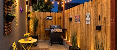 An outdoor patio with a barbecue grill, seating area, and a wooden fence.