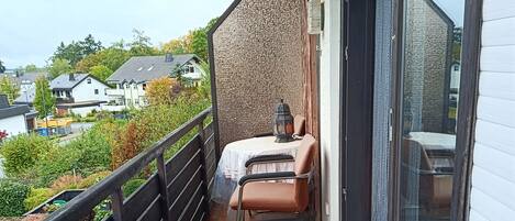 Ein Balkon mit Stuhl und Tisch, Blick auf Häuser und ein Fliesenboden.