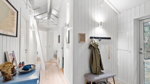 A hallway with white wooden walls, a bench with shoes, and a coat rack with a jacket. - Beautiful home in Blokhus with sauna (Blokhus)
