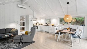 A spacious living area with a sofa, armchair, and dining table, featuring a large window and a ceiling fan. - Beautiful home in Blokhus with sauna (Blokhus)