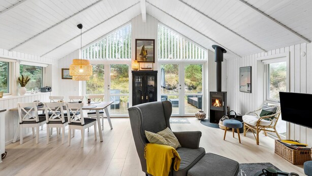 A spacious living area with a high ceiling, a fireplace, and large windows offering a view of the outdoors. - Beautiful home in Blokhus with sauna (Blokhus)
