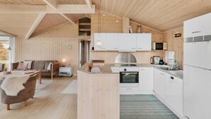 A modern kitchen with white cabinets, a Bosch refrigerator, and a microwave. There is a wooden dining table with a white furry chair. - Nice home in Væggerløse with WiFi (Væggerløse)