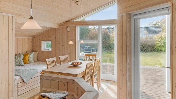 A wooden cabin interior with a dining area, a sofa, and a view of the outdoors. - Nice home in Væggerløse with WiFi (Væggerløse)