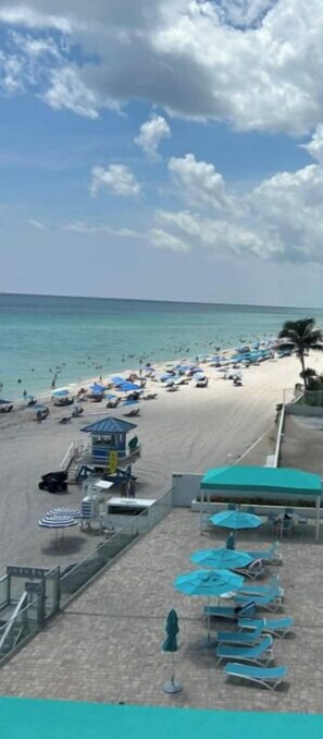 A beach with sun loungers and umbrellas, a lifeguard tower, and a clear view of the ocean. - Panoramic Beachfront Views! (Hollywood)