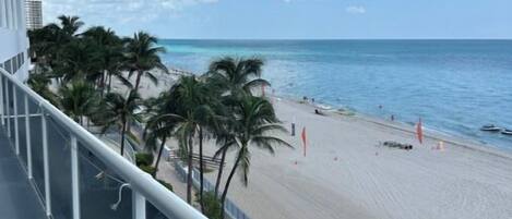 A balcony with a view of a beach, palm trees, and the ocean.