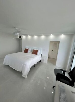A modern bedroom with a bed, a desk with a keyboard, and a ceiling fan. - Panoramic Beachfront Views! (Hollywood)