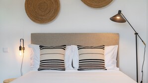 A neatly made bed with striped pillows, a wall-mounted lamp, and two woven wall hangings.