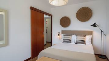 A hotel room with a bed, a bedside lamp, a woven bench, a large mirror, and two woven wall decorations.