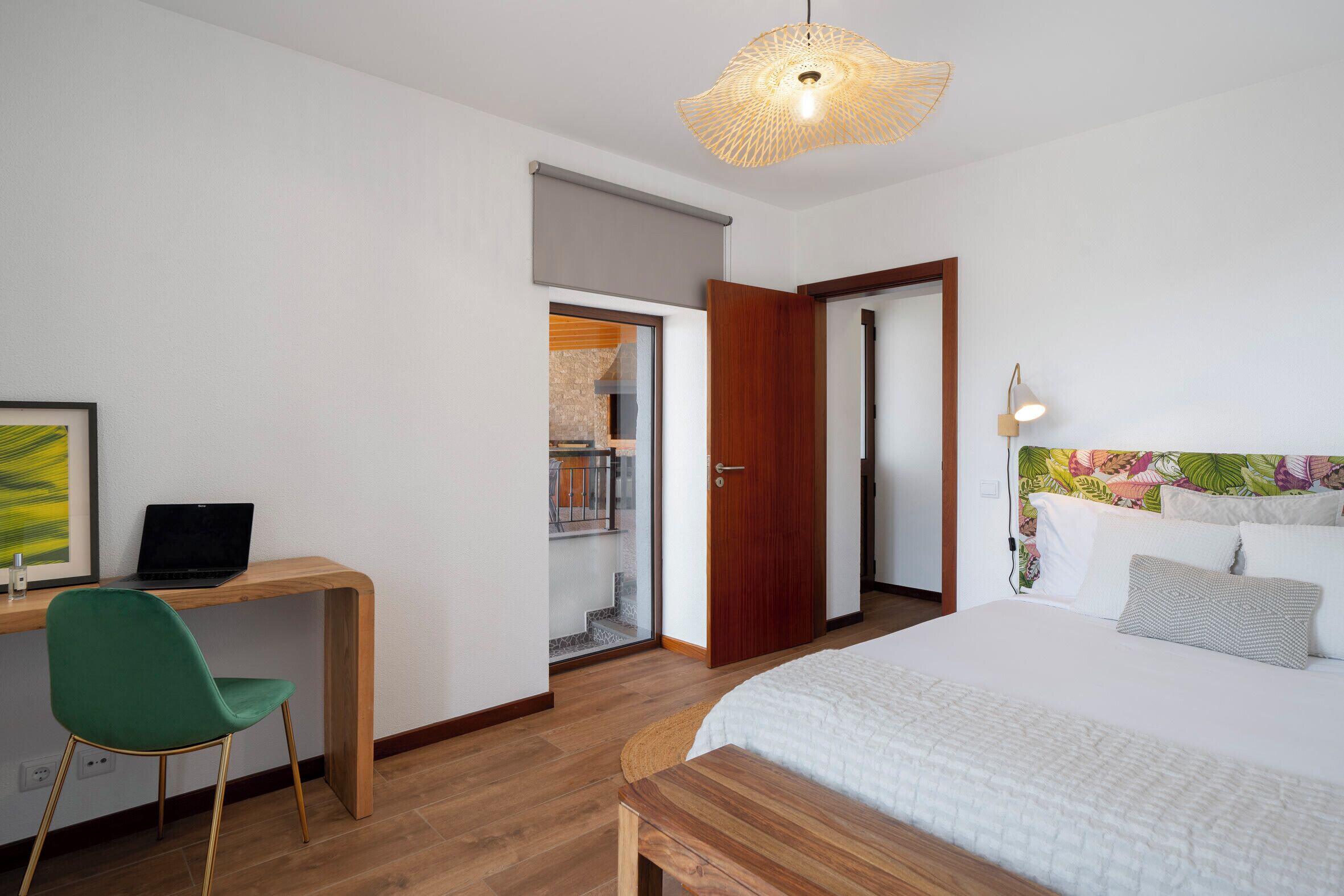 Un dormitorio con una cama, un escritorio con una computadora portátil, una silla y una puerta que da a un balcón.