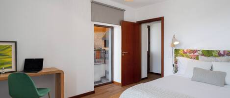 Un dormitorio con una cama, un escritorio con una computadora portátil, una silla y una puerta que da a un balcón.