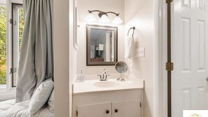 Un baño con lavamanos blanco, un espejo y una ventana con cortinas.