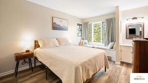 Un dormitorio con cama, mesita de noche, asiento junto a la ventana y un espejo.