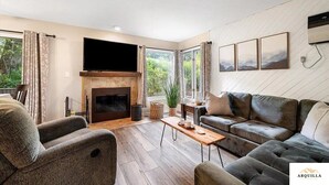 Una sala de estar con chimenea, un sofá, una televisión y un ventanal con cortinas.