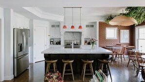 Une cuisine moderne dotée d’un îlot central, d’appareils électroménagers en acier inoxydable et d’un coin repas avec des chaises en bois et un luminaire suspendu.