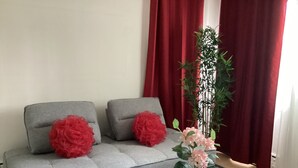 A grey sofa with two red pillows, a black and white checkered coffee table, and a potted plant with pink flowers. - Bright cosy apartment short walk to metro green line near Olympic Village    (Montréal)