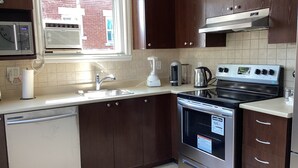 A modern kitchen with dark wooden cabinets, a stainless steel dishwasher, a built-in oven, and a window providing natural light. - Bright cosy apartment short walk to metro green line near Olympic Village    (Montréal)