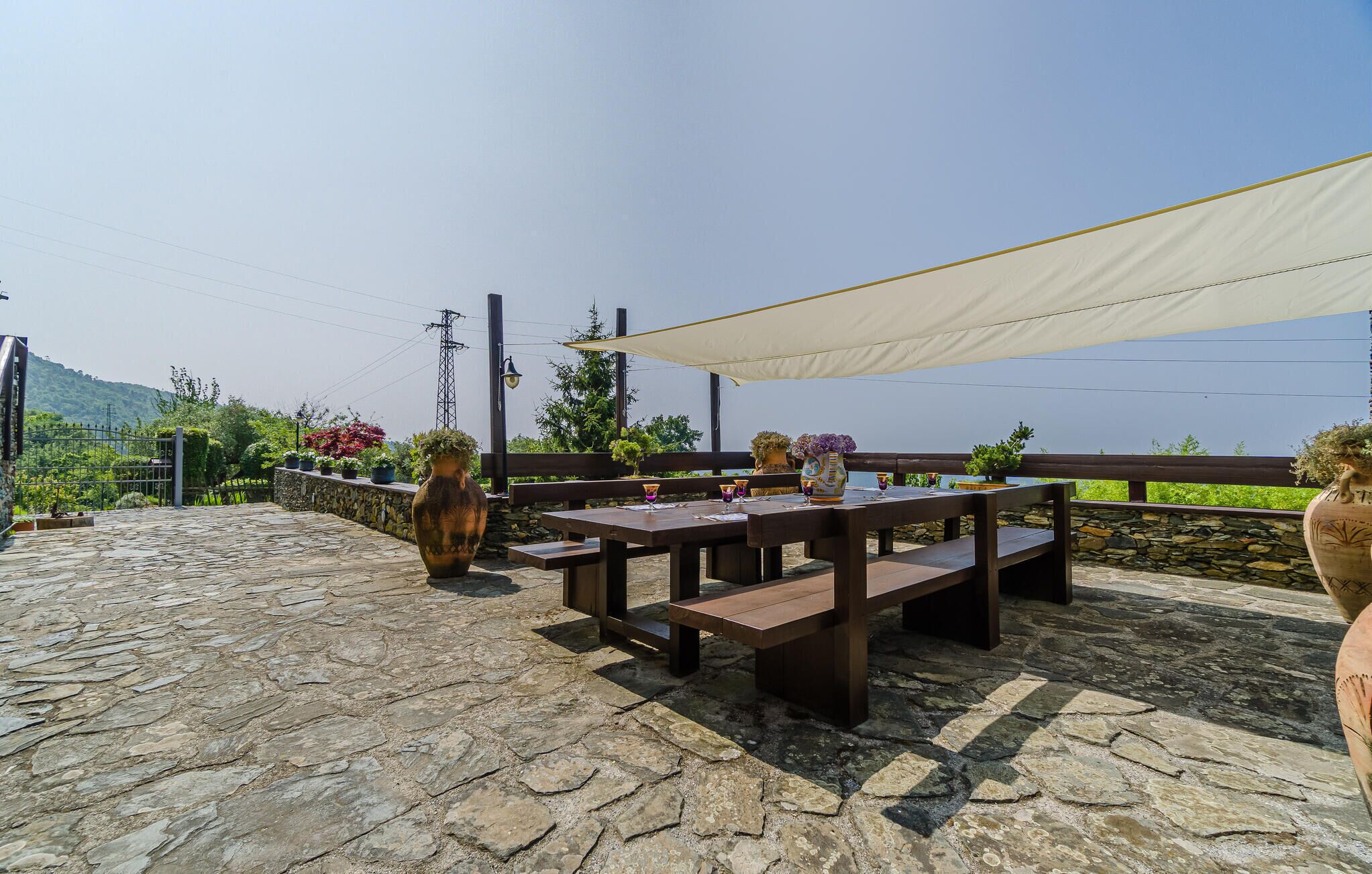 An outdoor patio with stone flooring, wooden benches, and a table set with glasses and a vase.