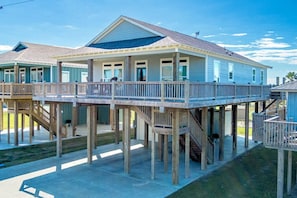 A beachfront house with a deck, multiple windows, and a covered porch.