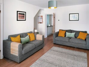 A modern living room with two grey sofas, a wooden side table, a patterned rug, and a ceiling light. - 2 bedroom accommodation in Warkworth (Warkworth)