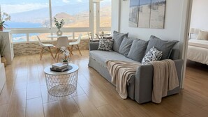 En moderne stue med en grå sofa, et rundt sofabord og havudsigt gennem store vinduer.
