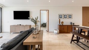 En moderne stue med sofa, et træspisebord, et fjernsyn ophængt på væggen og et køkken med træskabe.