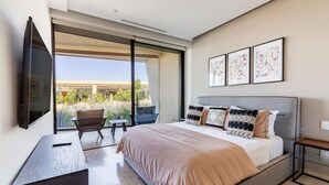 Una camera da letto moderna con un grande letto, una televisione a schermo piatto, una scrivania e una sedia. Tre opere d'arte incorniciate adornano la parete e si apre una vista sul verde esterno.