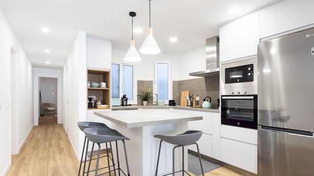Una cucina moderna con isola centrale, sgabelli da bar, elettrodomestici in acciaio inossidabile e illuminazione a sospensione.